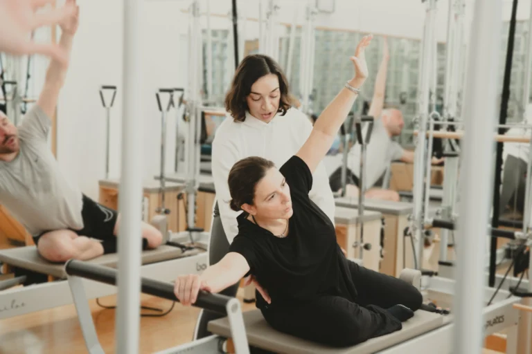 Instructora de pilates corrigiendo la postura de una alumna durante ejercicio lateral en máquina reformer en Siamo Pilates Madrid