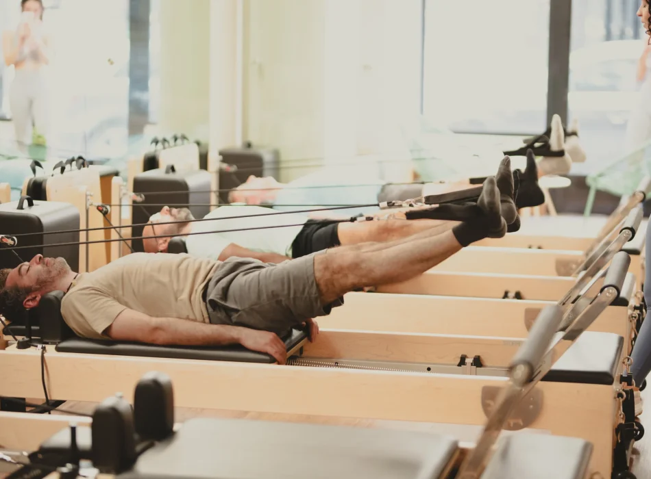 Sesión de pilates reformer para hombres en Madrid Hombres realizando ejercicios de pilates reformer guiados por instructora en Siamo Pilates Madrid