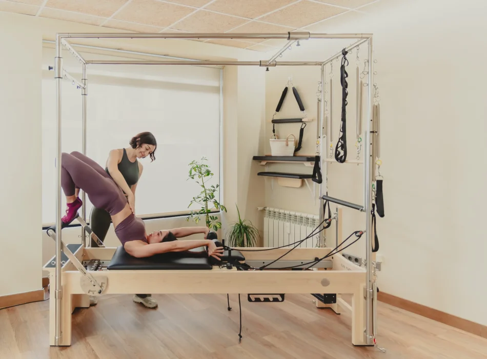 Sesión de pilates asistido con torre Cadillac Instructora de pilates asistiendo a alumna durante ejercicio en máquina torre Cadillac en el estudio Siamo Pilates de Madrid