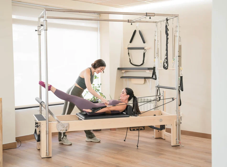 Instructora de pilates asistiendo a alumna durante ejercicio con Cadillac reformer en Siamo Pilates Madrid