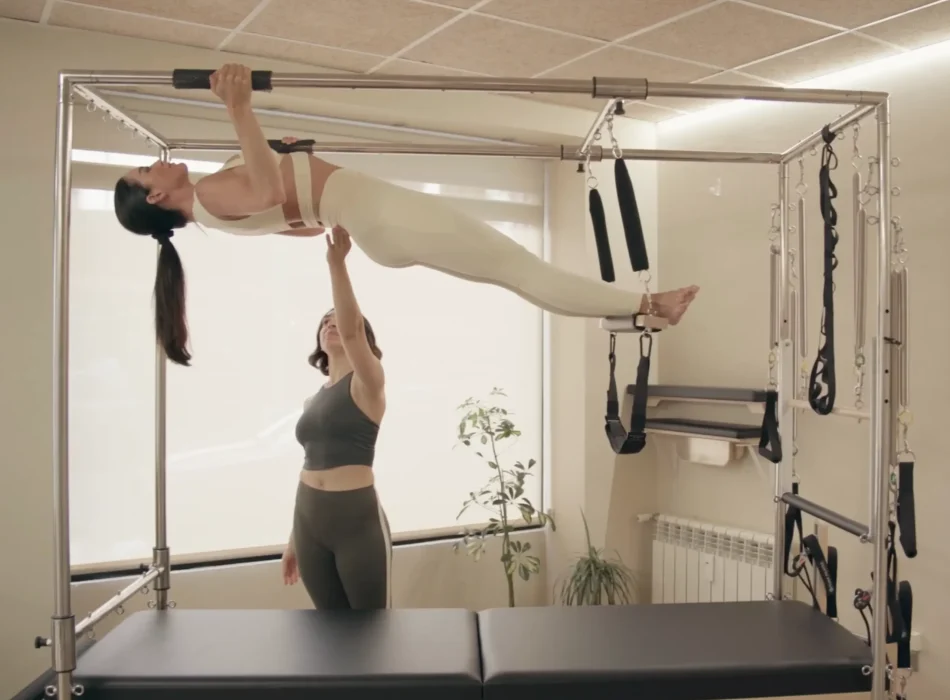 Pilates con Cadillac – Técnica avanzada con asistencia en Siamo Pilates Madrid Alumna realizando ejercicio avanzado en Cadillac con asistencia de instructora en Siamo Pilates Madrid