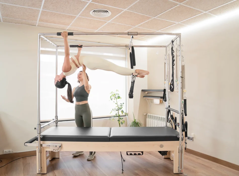 Entrenamiento personalizado con asistencia profesional en pilates Entrenadora asiste a alumna durante ejercicio de pilates avanzado en trapecio en Siamo Pilates Madrid